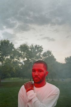 a man standing in the grass with his hands on his chest and red light coming from behind him