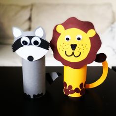 two paper animals sitting on top of a table next to each other, one with a lion face and the other with a raccoon's head