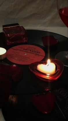 a table topped with candles and records on top of a black table covered in red hearts