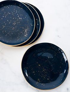 two black plates with gold speckles sit on a white marble countertop next to each other