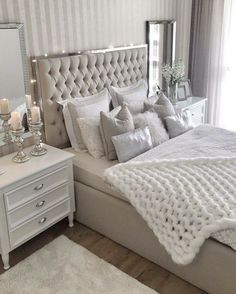 a bedroom with a white bed and lots of pillows on the headboard, along with candles