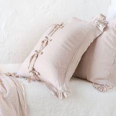 two pillows on top of a bed with white sheets and ruffle trimmings