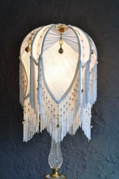 a white lamp with fringes hanging from it's side on a table next to a wall