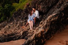 a man and woman are sitting on rocks by the water