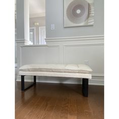 a white bench sitting on top of a hard wood floor next to a painting hanging on the wall