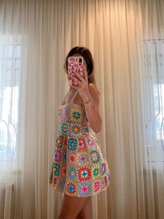 a woman taking a selfie in front of a window wearing a colorful dress and holding a cell phone up to her face