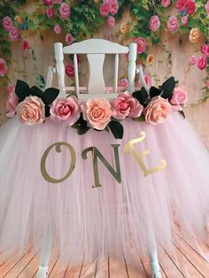 a white chair with pink flowers on it and the word one is spelled out in gold