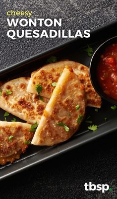 two quesadillas on a black plate with salsa in a bowl next to it