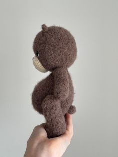 a hand holding a small brown teddy bear