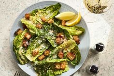 a white plate topped with lettuce and croutons next to a glass of wine