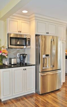 a kitchen with white cabinets and stainless steel refrigerator freezer combo in the center, along with hardwood flooring