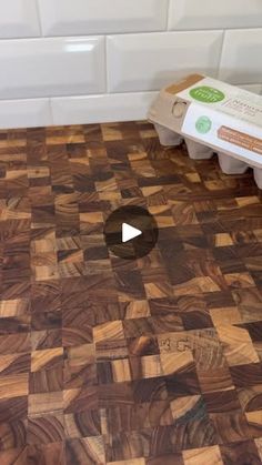 a wooden cutting board with an egg carton on the floor next to it and a video player