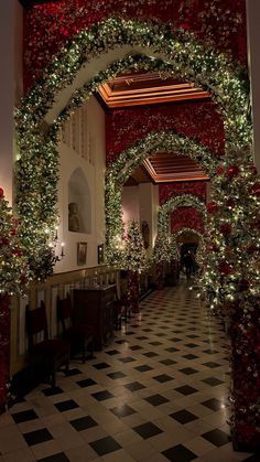 an archway decorated with christmas trees and garlands at the end of a hallway in a building