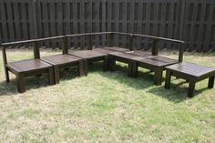 a wooden bench sitting on top of a grass covered field next to a black fence