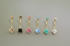 five different colored jeweled nose rings on a gray surface with one black, one pink, one blue and one green