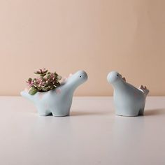 two ceramic dinosaurs with pink flowers in their mouths on a white countertop next to each other