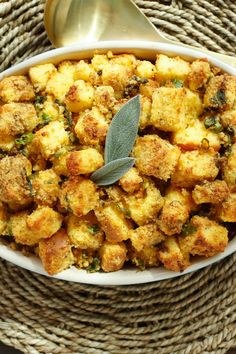 a white bowl filled with stuffing next to a metal spoon on top of a woven place mat