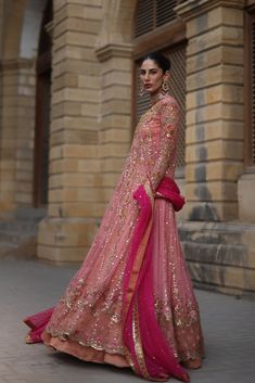 a woman in a pink and gold lehenga standing on the side of a building