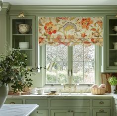 a kitchen with green cabinets and white counter tops has a window covered in floral roman shades