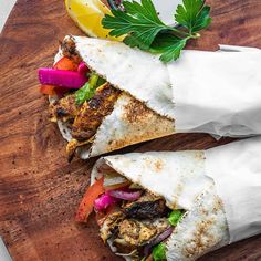 two burritos with meat and vegetables on a cutting board next to a lemon wedge