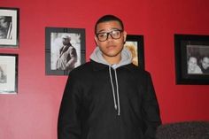 a young man standing in front of a red wall with pictures on the wall behind him