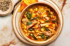 a bowl of chicken and chickpea soup next to some bread on a table