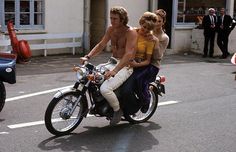 a man riding on the back of a motorcycle with a woman sitting on it's seat