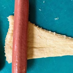 a long hot dog on a blue cutting board next to a doughnut roll with holes in it