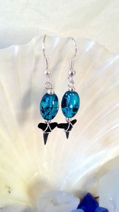 two blue glass beads with black bows hang from silver earwires on a white shell