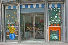 a storefront with flowers and bicycles painted on the front windows, along with potted plants