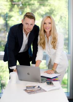 a man and woman standing next to each other in front of a laptop on a desk