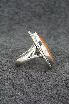 This spiny oyster and sterling silver ring was made by Navajo silversmith Chris Nez. The inside of the band is signed CN and stamped sterling.Size: 6.5Length: 1 1/4"Width: 1"Free shipping on all orders! We ship with USPS and always include tracking. All orders ship within a day of payment.Returns are accepted up to 30 days after you receive your order. Just send us a message. Our shop offers cash back or store credit. The item must be returned in new condition. Formal Orange Sterling Silver Rings, Sterling Silver Orange Ring With Polished Finish, Orange Sterling Silver Ring With Polished Finish, Orange Oval Sterling Silver Ring, Collectible Orange Sterling Silver Jewelry, Southwestern Style Rings With Polished Finish, Collectible Sterling Silver Opal Ring Stamped 925, Formal Sterling Silver Rings With Inlay, Spiny Oyster