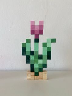 a green and pink plant sitting on top of a wooden block stand next to a white wall