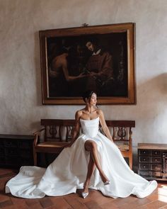 a woman is sitting on a bench in front of a painting and posing for the camera