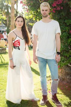 a man and woman standing next to each other in the grass with flowers behind them