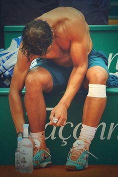 a shirtless tennis player sits on the bench with his knee bandage around his ankles