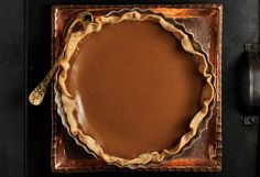 a chocolate pie with a golden spoon in it on a brown plate next to a black wall