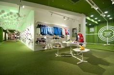 the inside of a sports shop with green carpet and white shelves filled with shirts, shoes and other items