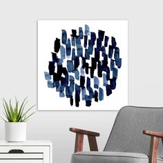 an abstract painting in blue and black on a white wall next to a gray chair