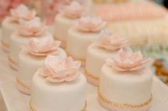 small white cakes with pink flowers on them are sitting on a table in front of other desserts