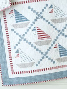 a blue and white quilt with sailboats on the front, red and white trim