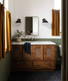 a bathroom with green and white tile, wooden cabinets and mirror above the sink is a potted plant