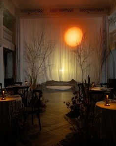 a dimly lit room with tables and chairs in the center, surrounded by tall trees