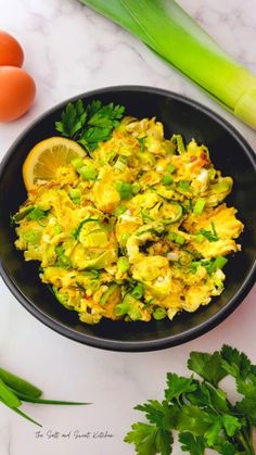 an egg salad in a black bowl next to green onions and celery on a white table