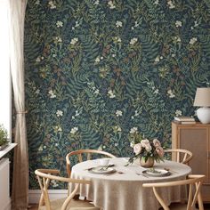 a dining room table with two chairs and a vase on it in front of a floral wallpaper