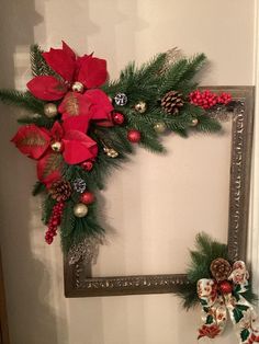 a christmas wreath with poinsettis and pine cones hanging on the wall next to a mirror