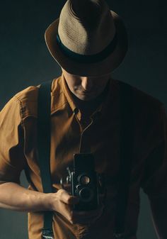 a man wearing a hat holding a camera in his right hand and looking at it