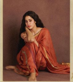 a woman sitting on the ground in a red sari with her hand under her chin