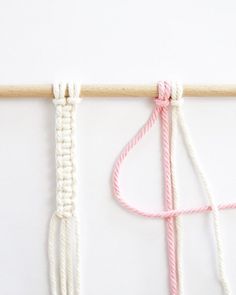 two pieces of pink and white yarn tied together on a wooden stick next to a pair of scissors