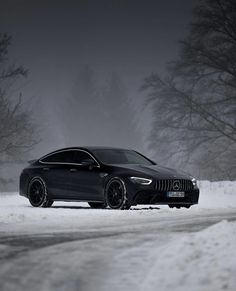 a black car parked on the side of a snow covered road in front of trees